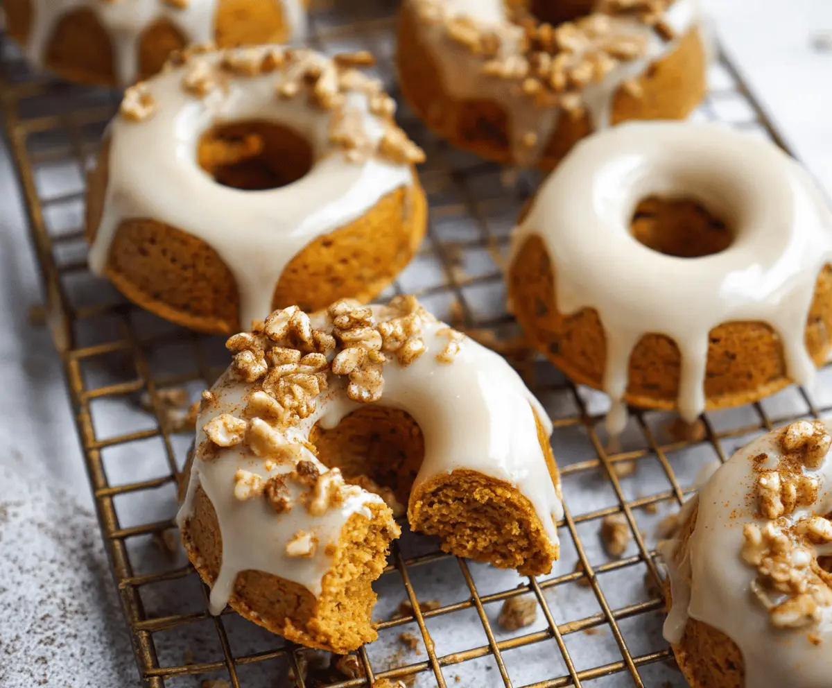 Delicious homemade pumpkin baked donuts topped with smooth maple glaze, served on a rustic plate with cinnamon and pumpkin seeds for a cozy fall treat.