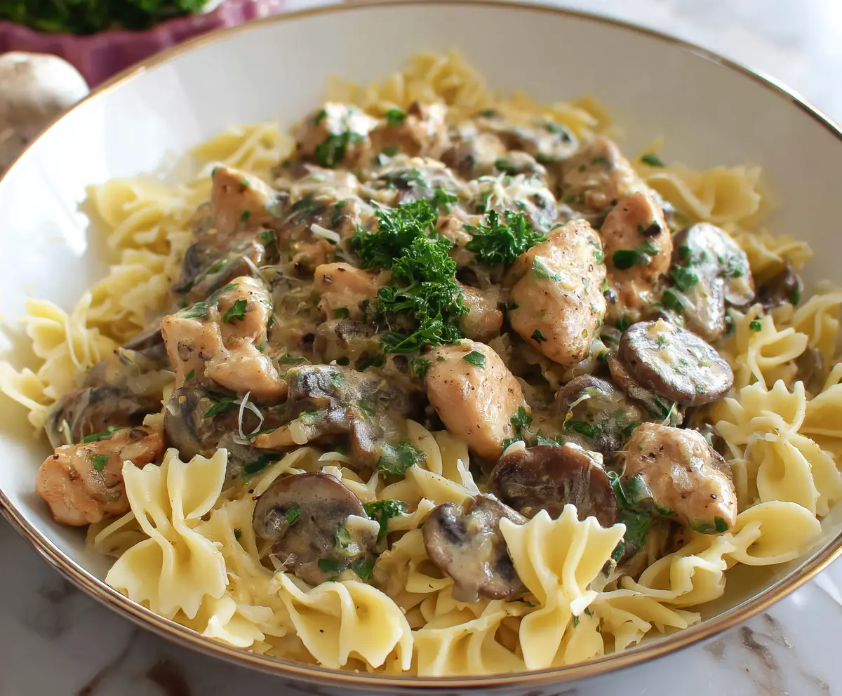 Creamy chicken and mushroom pasta served on a white plate, garnished with fresh herbs.