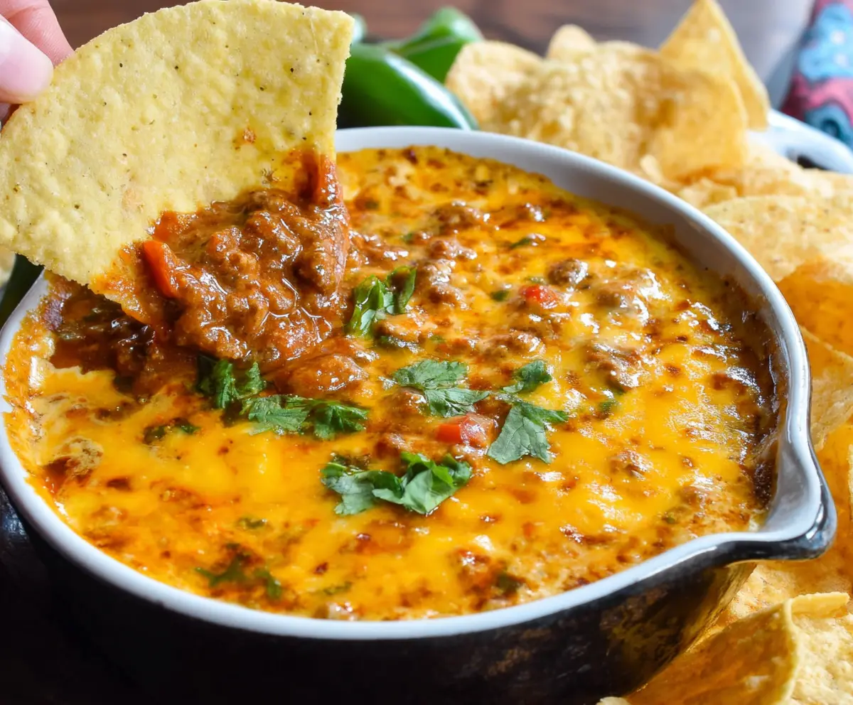 Delicious spicy chili cheese dip with melted cheese and toppings served in a bowl