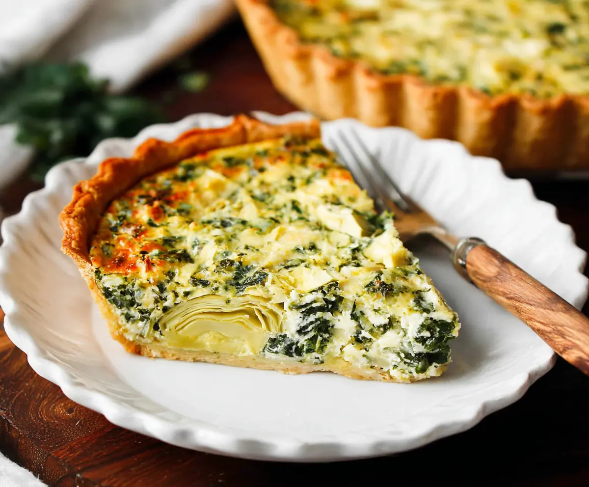 Delicious spinach and artichoke quiche sliced on a plate, garnished with herbs.