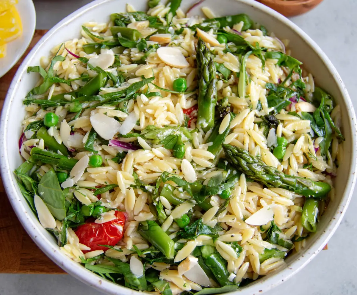 Colorful spring orzo pasta salad with fresh vegetables and herbs served in a vibrant bowl.