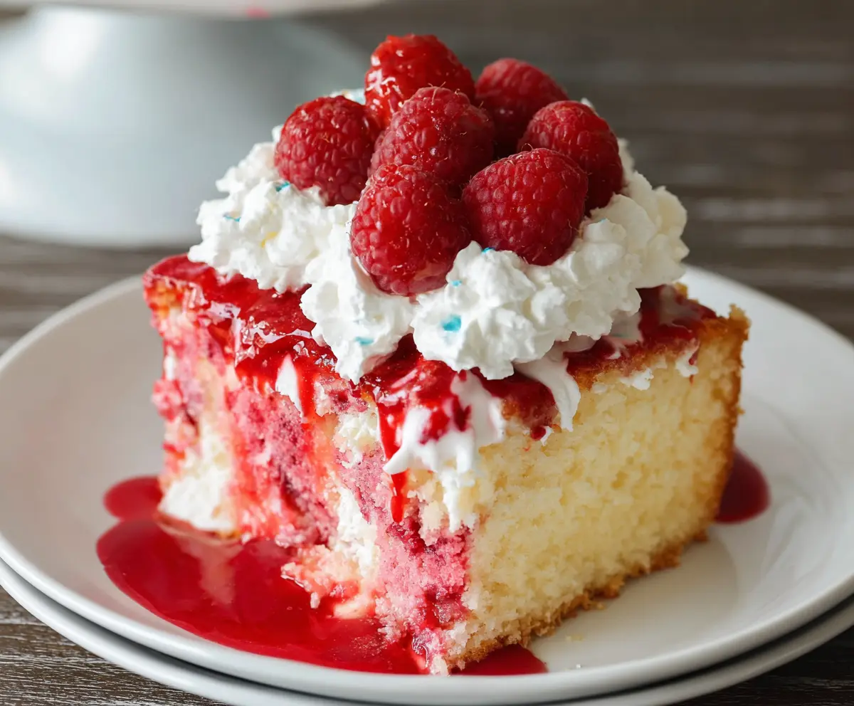 Delicious Raspberry Poke Cake with fresh raspberries and whipped cream topping.